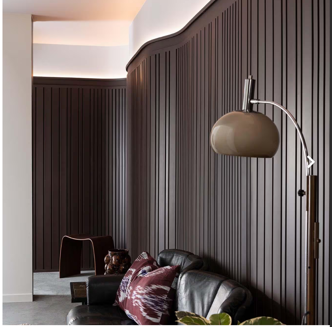 Full view of sculpted wall panels in a rich mahogany brown with architectural grooves, styled behind a black sofa and modern furniture.